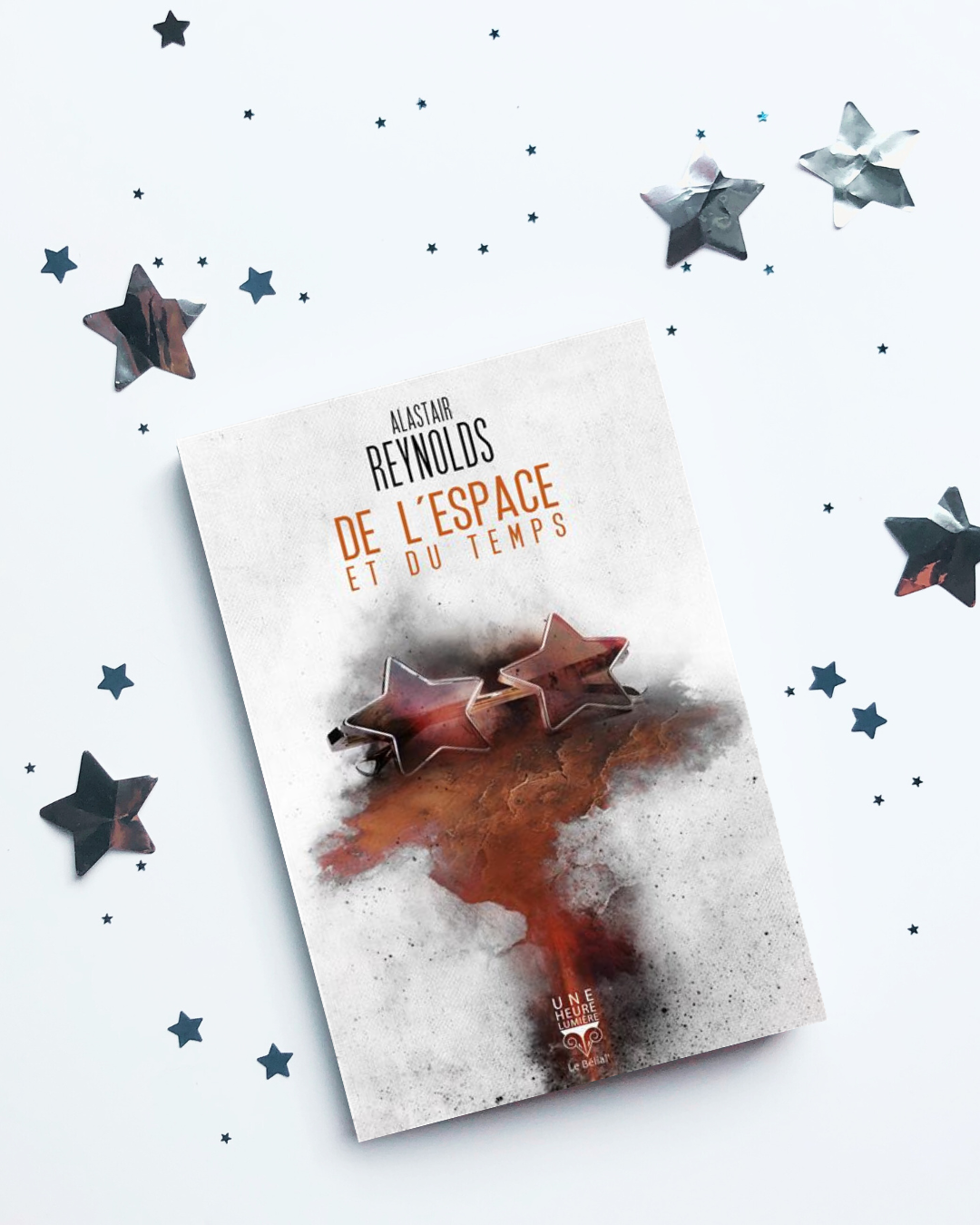 Livre posé sur une surface claire avec des étoiles éparpillées. La couverture de De l’espace et du temps montre une paire de lunettes en formes d’étoiles posée sur Mars. 